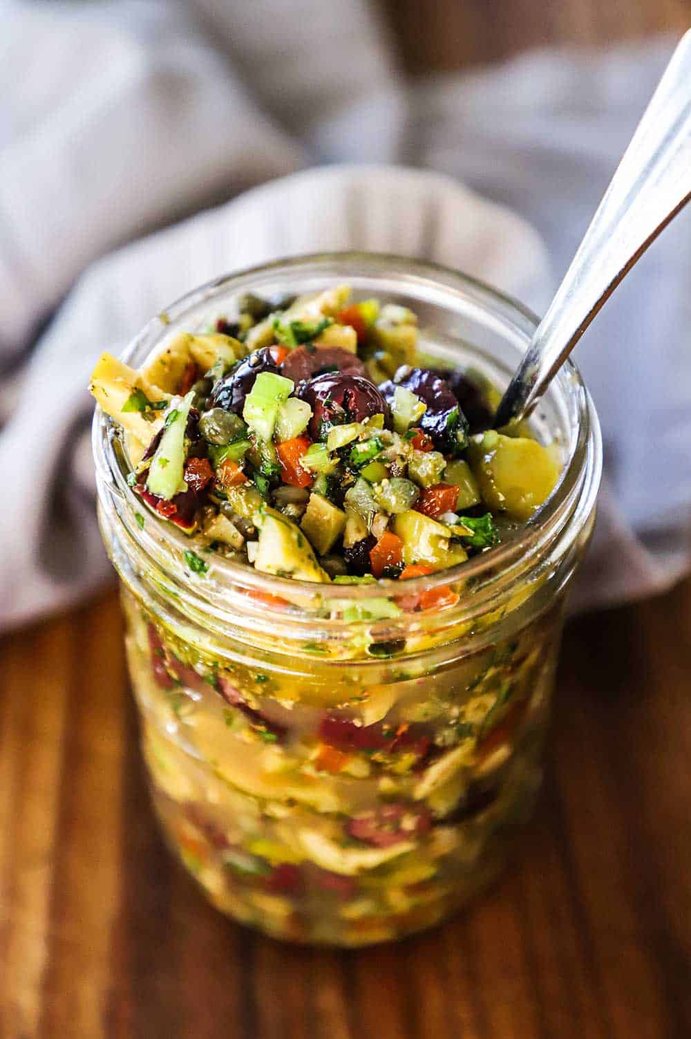 A mason jar filled with olive salad with a spoon inserted into it.