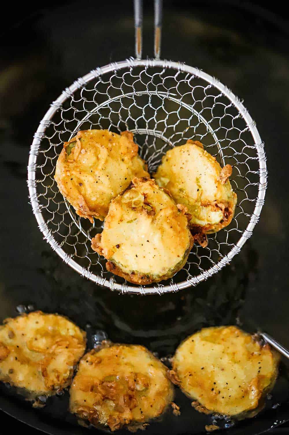A spider deep fryer catcher holding three fried pickles right out of the hot oil.