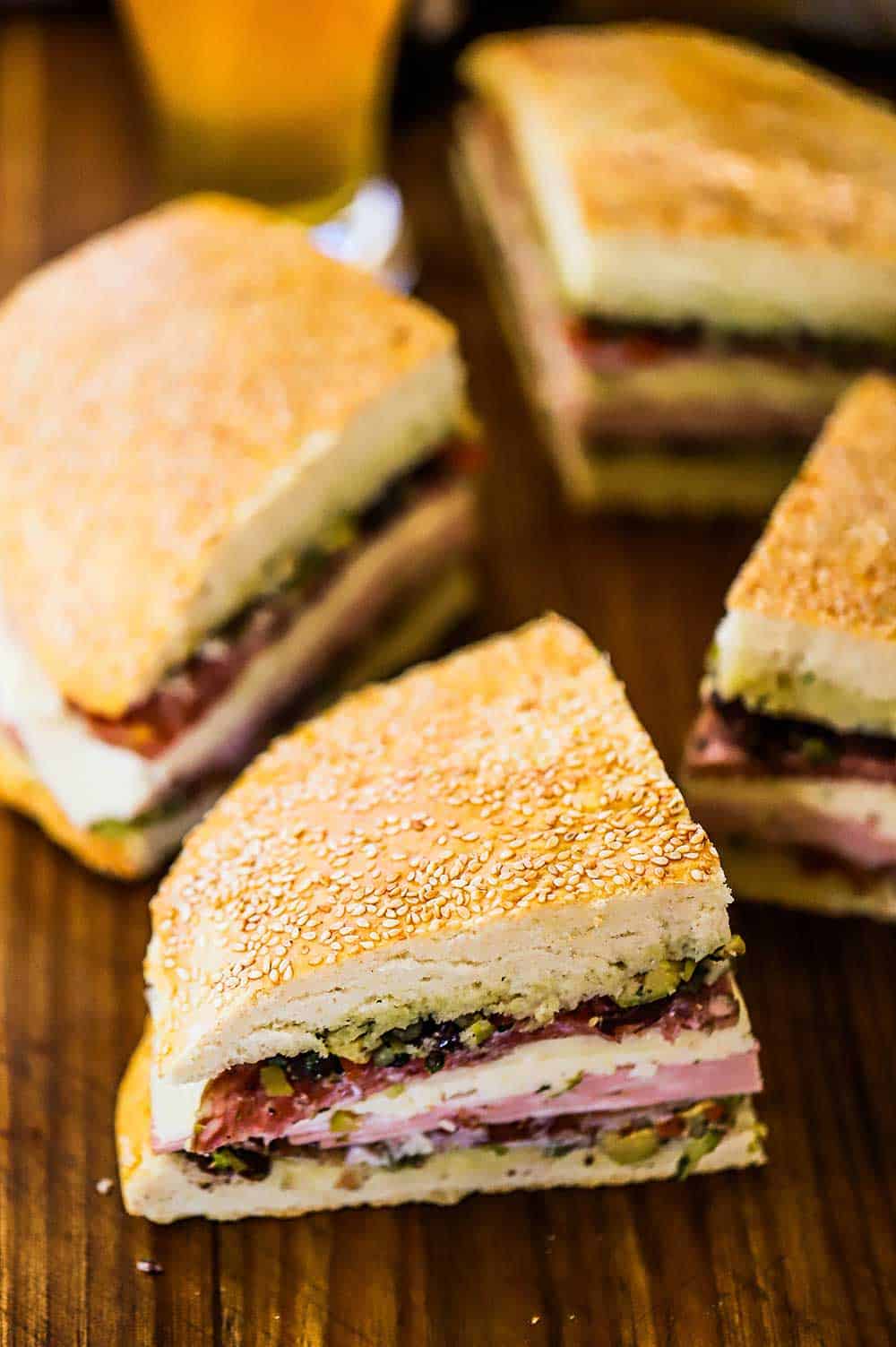 Four quarter pieces of a muffuletta sandwich sitting on a wooden cutting board.