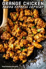 An overhead view of a wok filled with orange chicken with a wooden spoon inserted in the side.