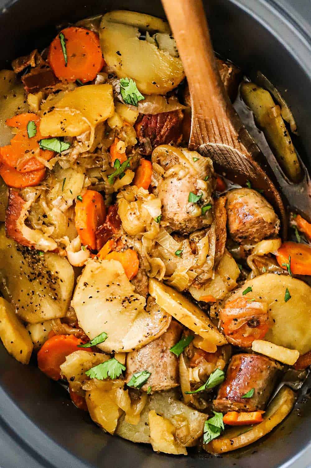 Dublin Coddle in a slow cooker with a wooden spoon stuck in the side.