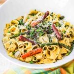 A circular white serving bowl filled with pappardelle with seasonal vegetables next to a bottle of Rosé and two glasses of wine.