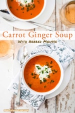 An overhead view of two white soup bowls filled with carrot ginger soup sitting next to a wine glass of Rosé.