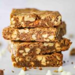 Four blondies with vanilla chips and toffee stacked on top of each other on a piece of white parchment paper.