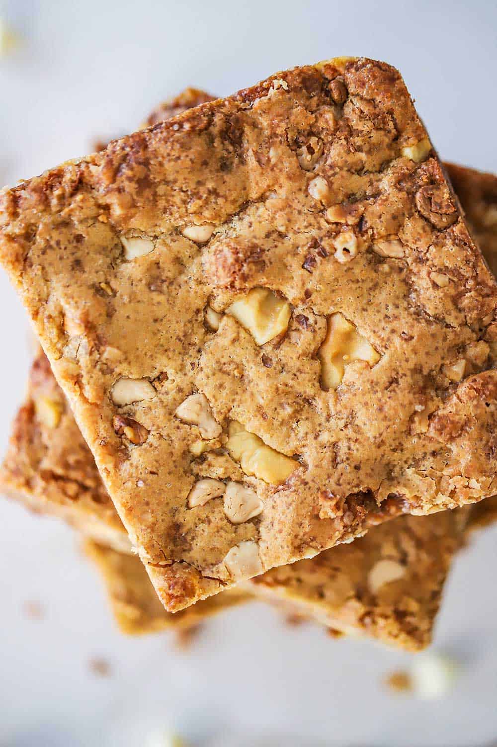 An overhead view of a stack of blondies that are studded with walnuts, white chocolate morsels, and toffee.