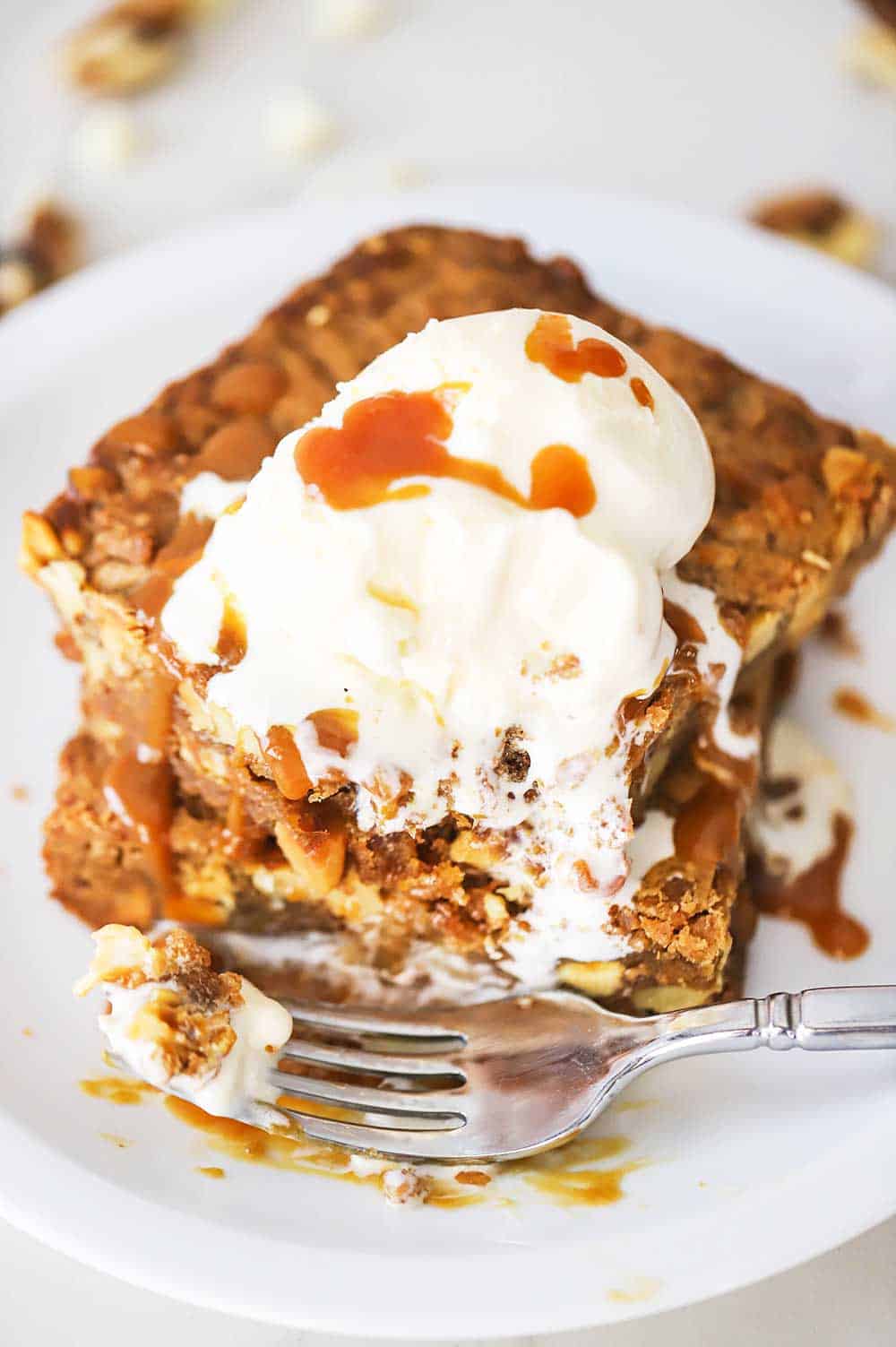 A white dessert plate filled with two blondies stacked on top of each other with a partially melted scoop of vanilla ice cream on top with a fork sitting next to it.
