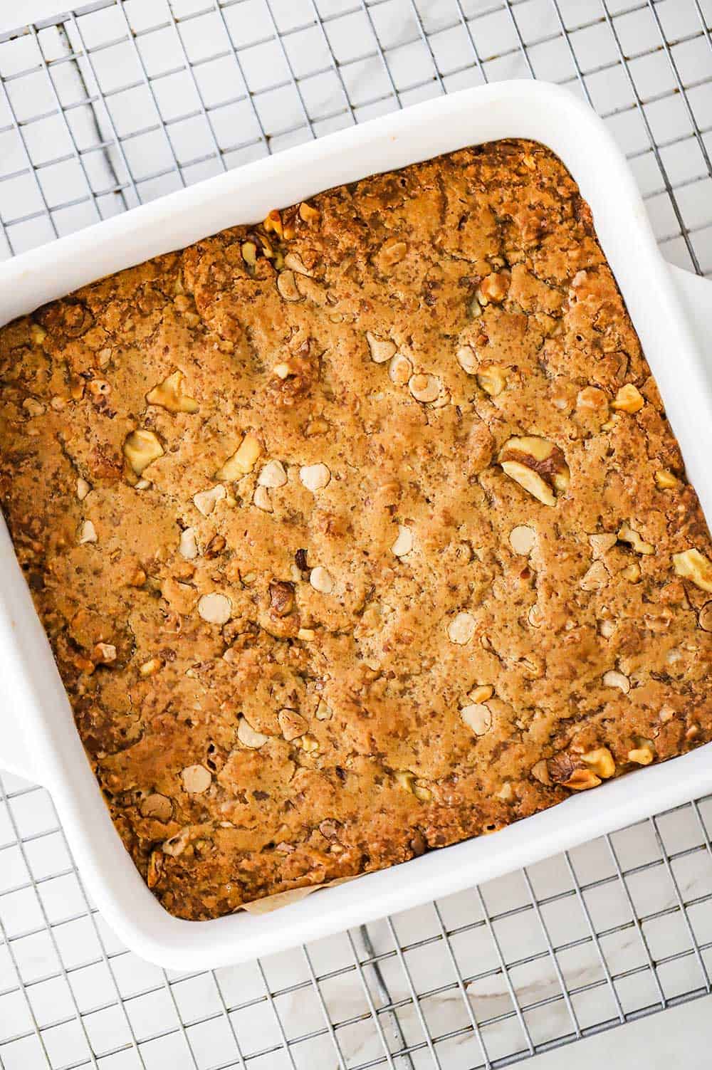 An overhead view of a square white baking dish filled with freshly baked blondies sitting on a wire baking rack.