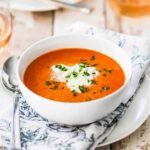 A single white soup bowl filled with carrot ginger soup topped with an herb mousse.