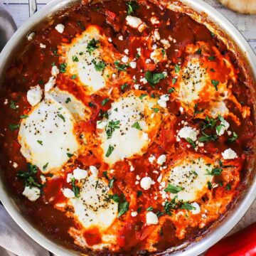 An overhead view of a large stainless steel skillet filled with poached eggs in a vibrant red tomato sauce.