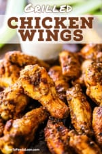 A close-up view of grilled chicken wings with buffalo sauce piled high next to a jar of blue cheese dressing.