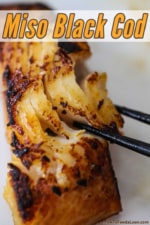 A close-up view of a pair of chop stick flaking a piece of black cod that has been fully cooked