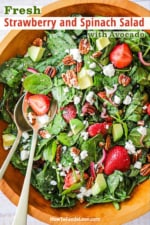 An overhead view of a fresh strawberry spinach salad with avocado that has been tossed together in a wooden bowl.