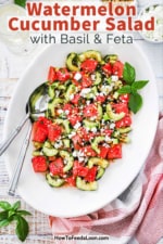 An overhead view of a large white oval platter filled with a watermelon cucumber salad with basil and feta.