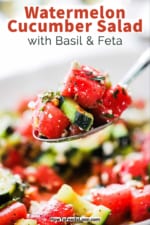 A large silver spoon lifting up a helping of watermelon cucumber salad with basil and feta.