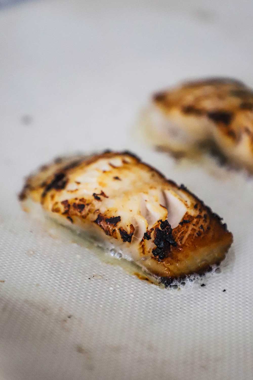 A baked strip of black cod on a silicone mat on a baking pan.