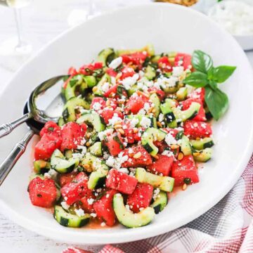 A large white oval platter filled with watermelon cucumber salad with feta and basil