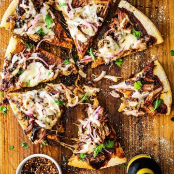 An overhead view of a grilled pulled pork pizza that has been cut into slices on a cutting board.