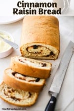 A loaf of cinnamon raisin bread that has three slices cut and are sitting on parchment pater next to a serrated knife and a bowl of softened butter.
