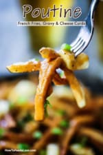 A fork holding up several french fries that are coated with brown gravy.