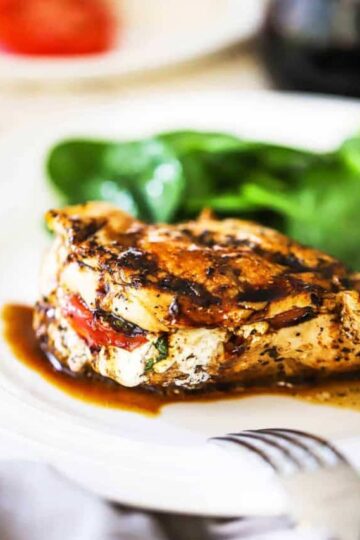 A close-up view of a caprese-stuffed chicken breast with a balsamic glaze on a white dinner plate.