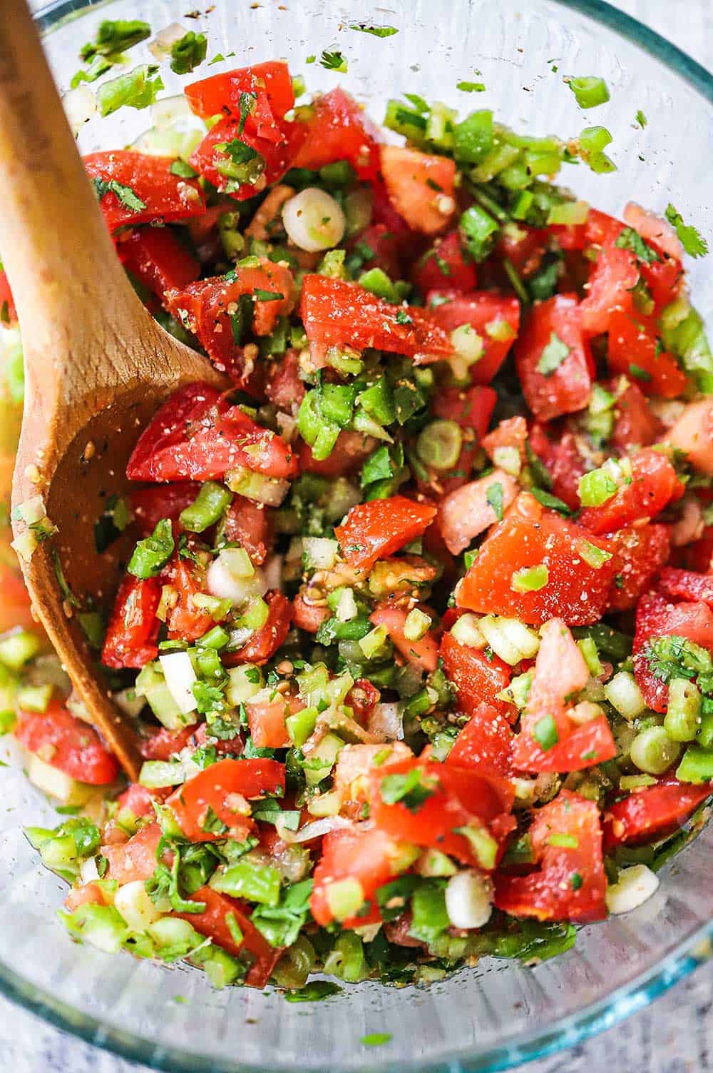 A glass bowl filled with Santa Maria salsa and a large wooden spoon. 
