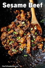 An overhead view of a wok that is filled with sesame beef and a wooden spoon off to the side.