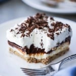 A square serving of layered chocolate delight sitting on a white plate with a bite missing.