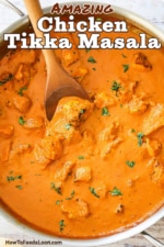 An overhead view of a large silver saucepan filled with creamy chicken tikka masala with a wooden spoon resting in the sauce.