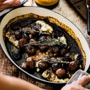 A person holding onto the sides of an oval baking dish that is filled with seared haddock with agrodolce sauce