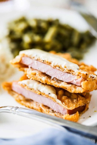A Southern-fried pork chop that has been cut in half and one half is sitting on top of the other.