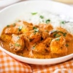 A close-up view of a white bowl with a helping of chicken tikka masala and steamed white rice in it.