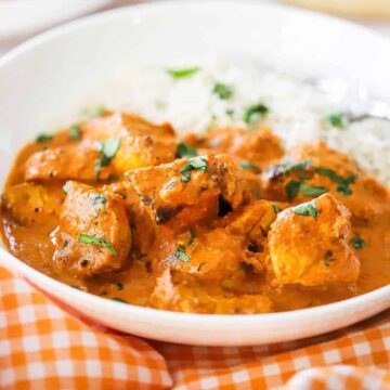 A close-up view of a white bowl with a helping of chicken tikka masala and steamed white rice in it.