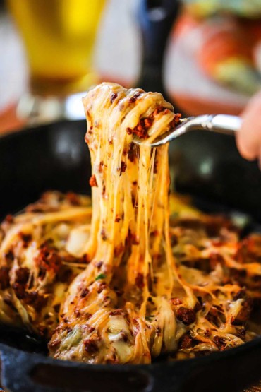 A person using a fork to pull melted cheese and cooked chorizo from a cast-iron skillet