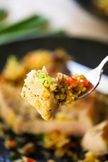 A fork being used to hold up a bite of a pork chop and Spanish rice.