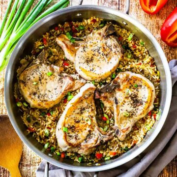 An overhead view of four pan-seared bone-in pork chops sitting in a large skillet of Spanish-style rice.