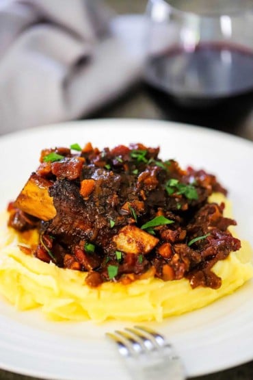 A plate of mashed potatoes topped with braised beef short ribs and a tomato vegetable sauce. 
