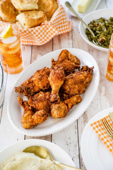 A platter filled with Southern fried chicken surround by bowls filled with green beans, mashed potatoes, and biscuits.