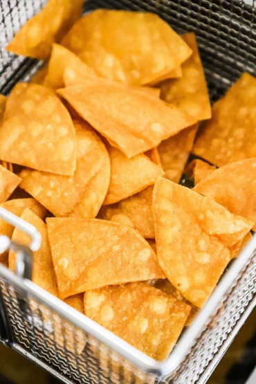 A fryer basket filled with freshly fried corn tortilla chips. 