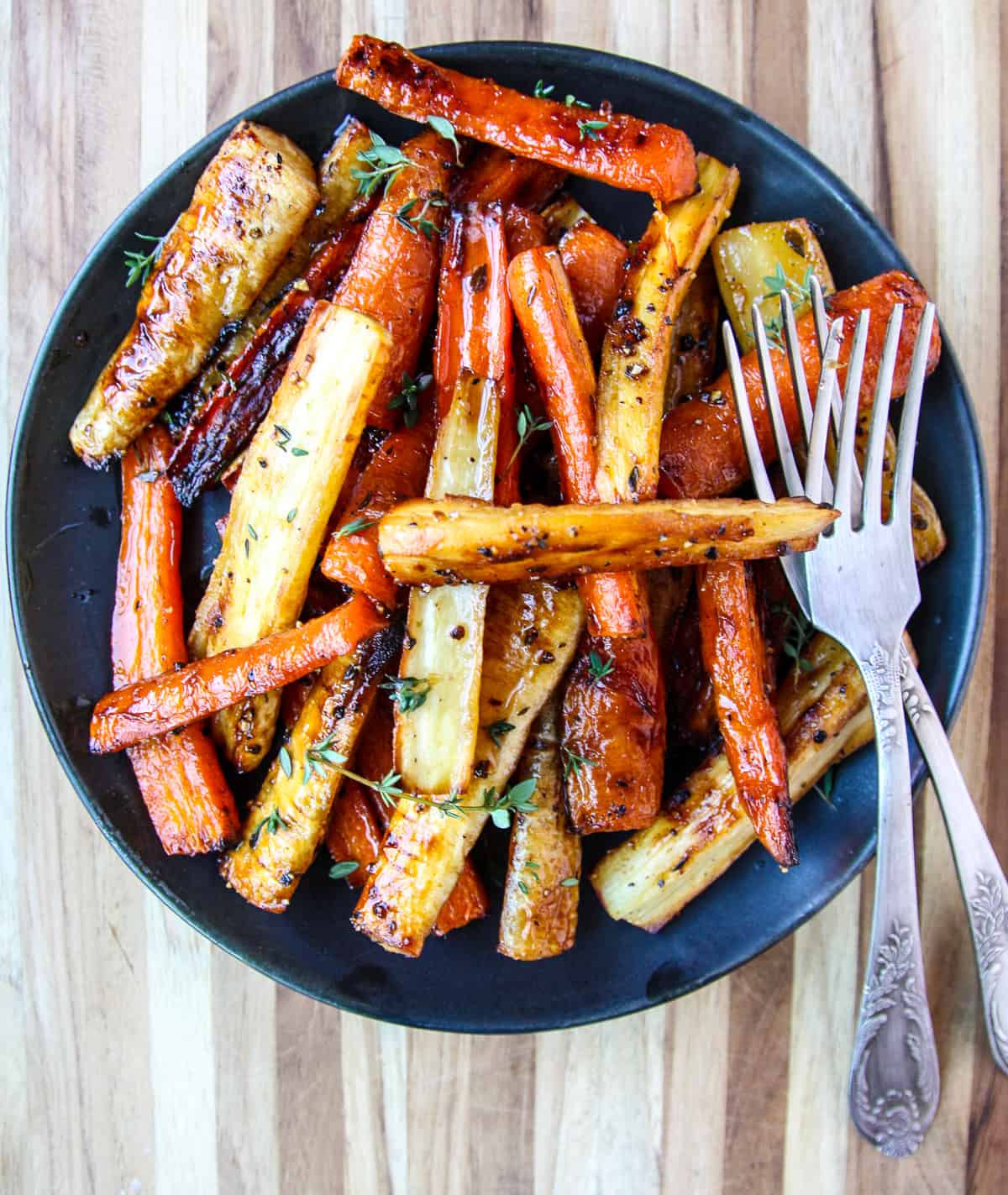 Honey roasted carrots and parsnips on a black plate.