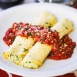 Two homemade stuffed manicotti topped with a strip of marinara sauce.
