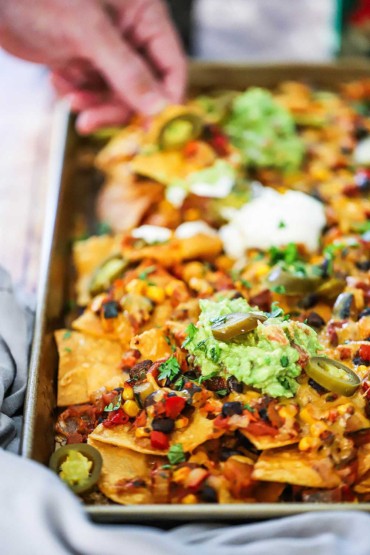 A person pulling a chili cheese nacho from a sheet pan filled with them. 