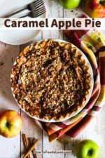 An overhead view of an unsliced caramel apple pie surrounded by whole apples and cinnamon sticks.