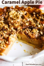 An apple pie with caramel in a white pie dish with a large piece missing.