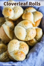 A close-up view of a basket lined with a blue cloth and filled with cloverleaf dinner rolls.