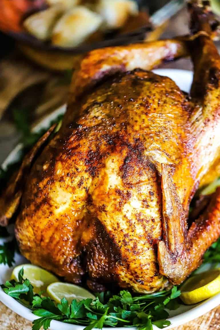 A deep-fried turkey sitting on a platter that is garnished with fresh parsley and lemon slices. 