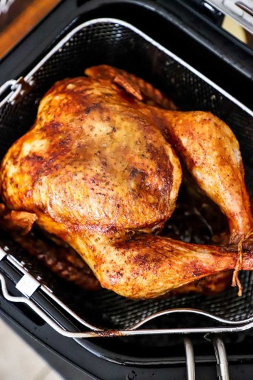 A freshly deep-fried turkey resting in the fryer basket above the hot oil on the electric fryer. 