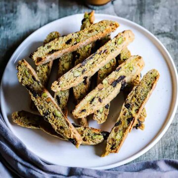 An overhead view of a white plate filled with a stack of pistachio and dried cherries biscotti.