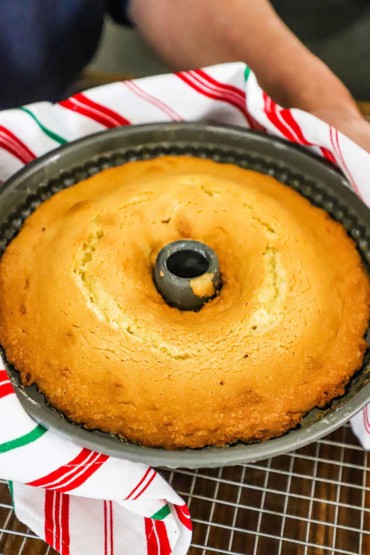 A person holding a bundt pan filled with a baked gold cake.