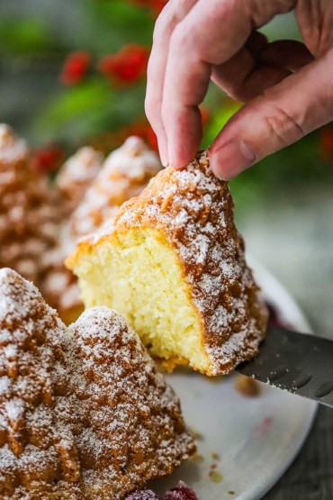 A person using a chef's knife to lift a slice of a Christmas bundt cake from the cake on a white plate.