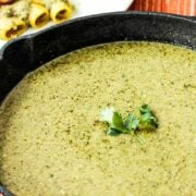 A black cast-iron skillet filled with pumpkin seed (Pipián) sauce with a sprig of cilantro in the middle.